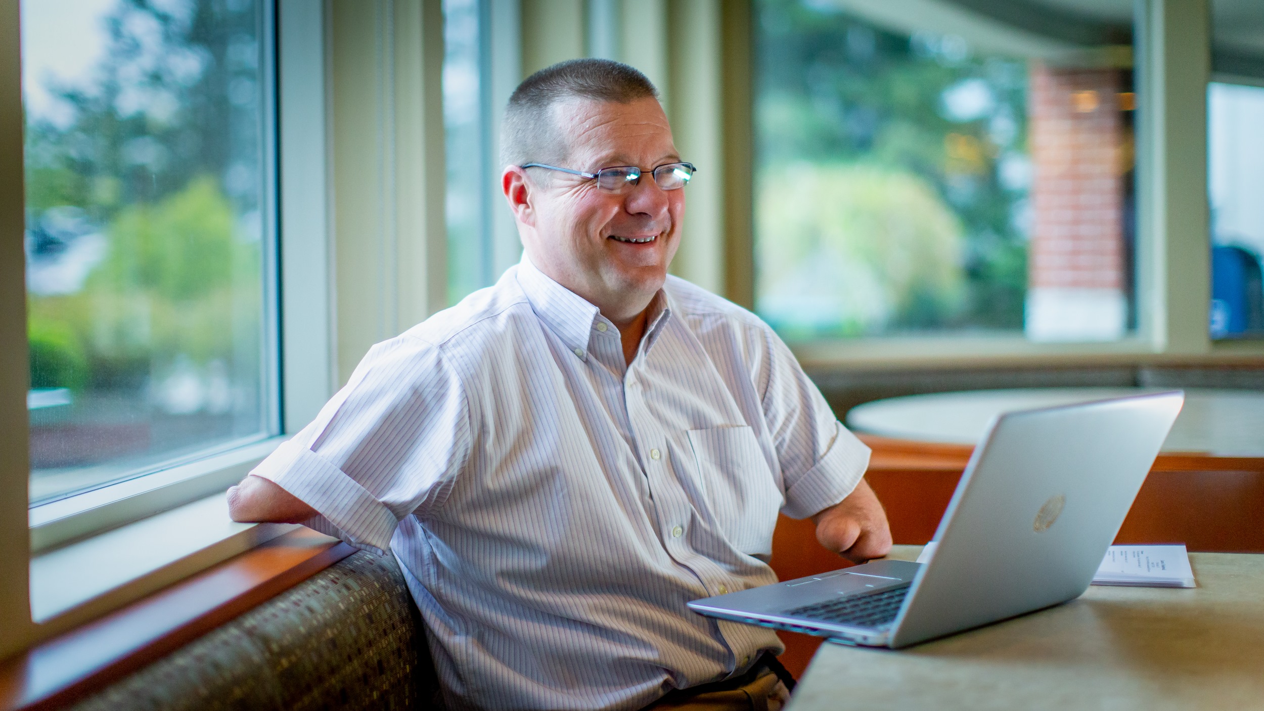 John Robinson, CEO de Our Ability sentado, sonriendo y frente a su computadora portátil