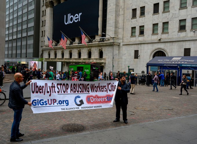 Dos conductores sostienen un cartel de protesta mientras la pancarta de Uber se cuelga en el frente de la Bolsa de Nueva York el 10 de mayo de 2019 en Nueva York.
