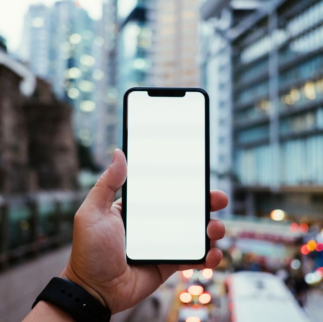 Recorta la mano del hombre que sostiene el teléfono móvil frente a los rascacielos urbanos en el distrito financiero del centro con tráfico de la ciudad ocupada