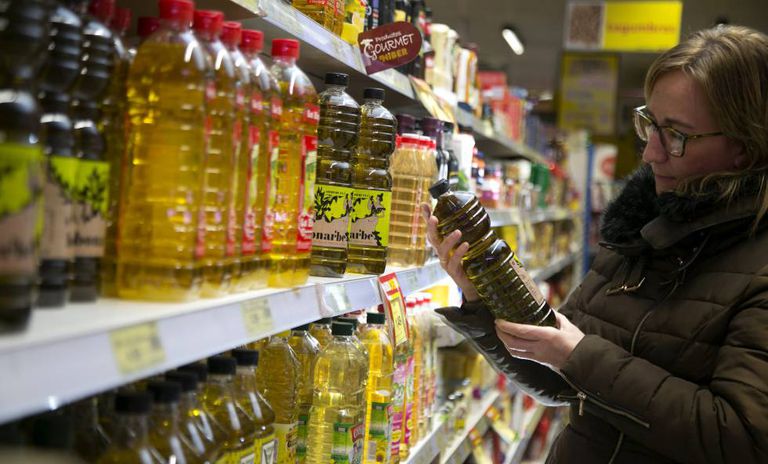 Una mujer mira varias botellas de aceite de oliva en un supermercado.