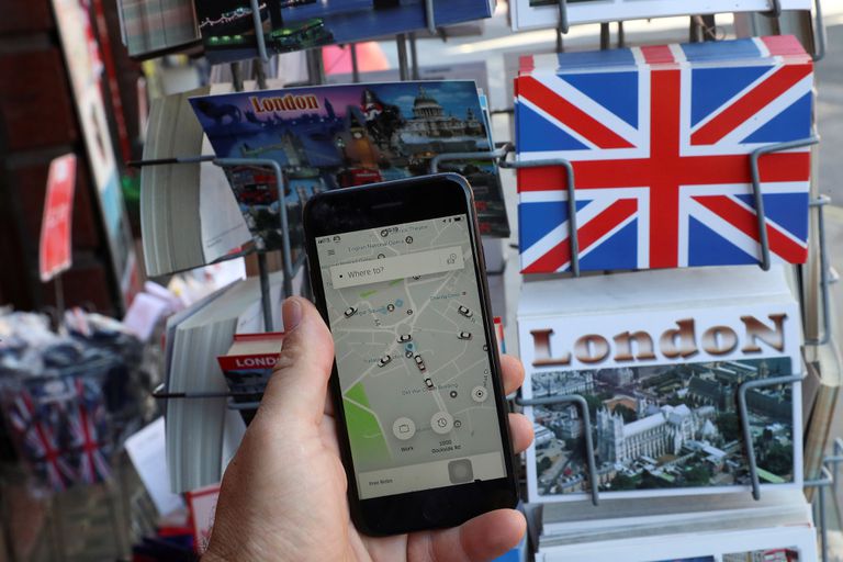 Un hombre utiliza la aplicación de Uber frente a una tienda de venta de postales turísticas en Londres.