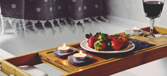 Bandeja de bañera de madera con velas, fresas y vino.