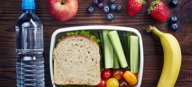 un almuerzo saludable de frutas, verduras, agua y un sándwich sobre una mesa