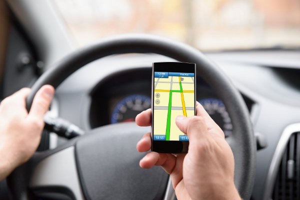 Un conductor con una mano en el volante y otra mano sosteniendo un teléfono inteligente con una aplicación de mapa abierta. 