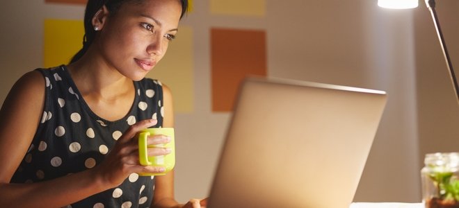 una mujer con una taza mira su computadora portátil por la noche