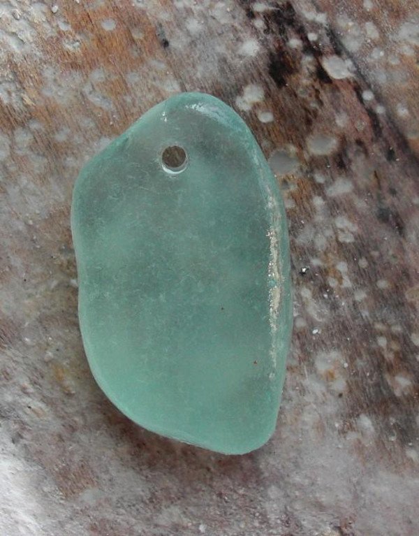 Un trozo de vidrio con un agujero en la parte superior para hacer un collar. 