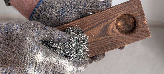 Manos aplicando lana de acero al candelabro de madera carbonizada