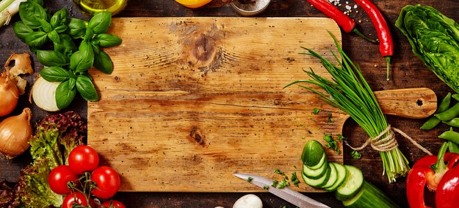 tabla de cortar de madera rodeada de hierbas y verduras