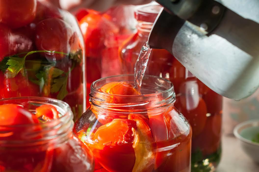 Verter agua en frascos de tomates para enlatar. 