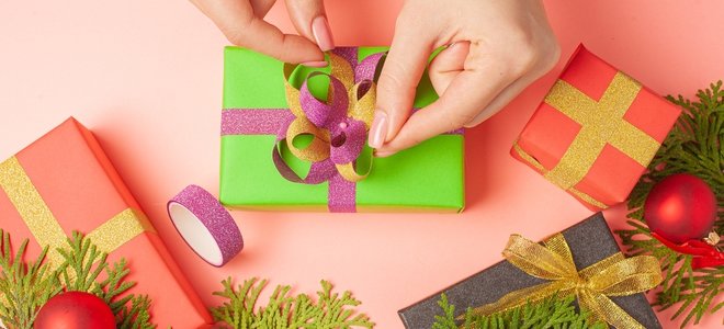 Manos atando cinta brillante en un regalo envuelto en verde con verduras navideñas cercanas