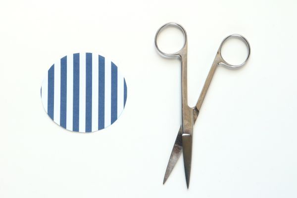 Un par de tijeras plateadas junto a un círculo de papel rayado azul y blanco. 