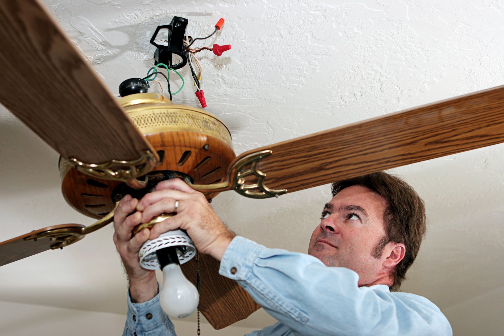 Un hombre instalando un ventilador de techo. 