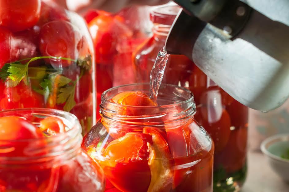 Se vierte agua caliente en frascos de vidrio llenos de tomates. 