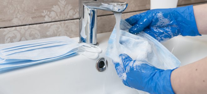 manos con guantes lavar una mascarilla con agua y jabón