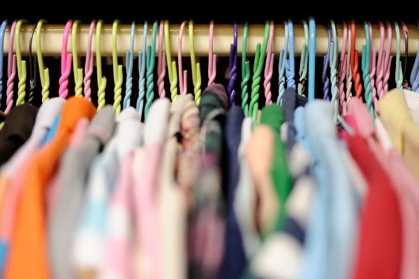 Una fila de perchas de colores y ropa en un armario. 