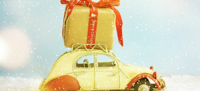 Un regalo de Navidad de gran tamaño encima de un coche vinatge de juguete en la nieve. 