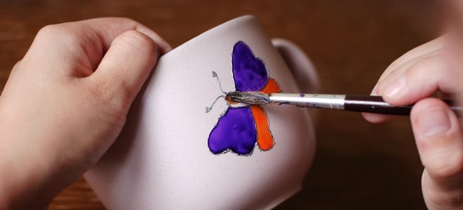 mano pintando una mariposa en una taza