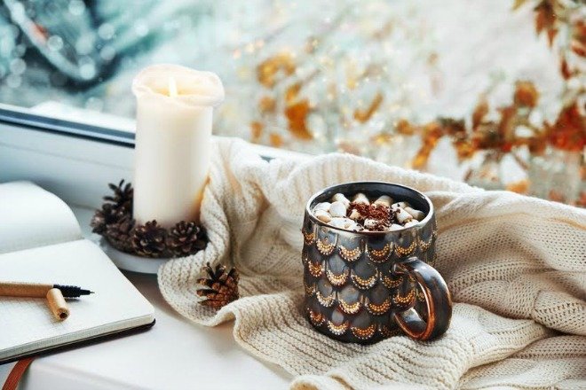 Una vela decorada con piñas con una taza de café y un libro. 