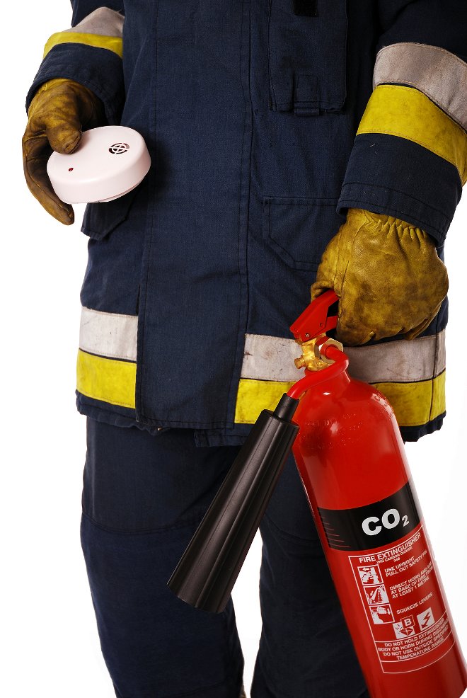 Un bombero sosteniendo una alarma de humo y un extintor de incendios. 