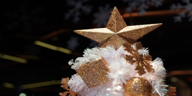 Estrella de brillo dorado y adornos en la parte superior de un árbol de Navidad blanco