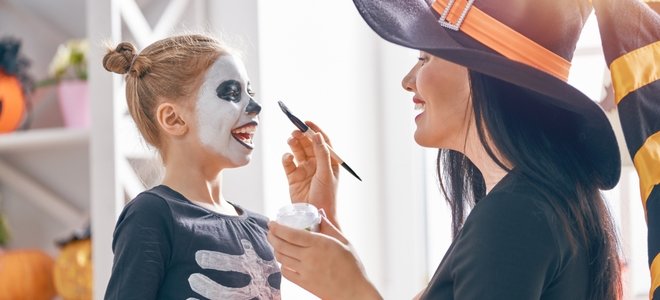 Mamá poniendo pintura facial en hija en disfraz de Halloween
