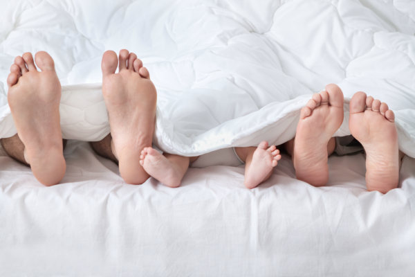 Tres pares de pies sobresaliendo de la ropa de cama blanca