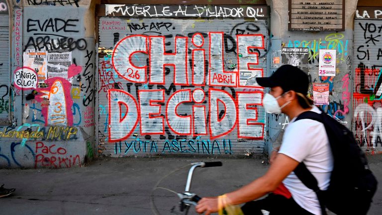 Un hombre en bicicleta pasa este viernes 23 de octubre delante de una pintada callejera que llama a votar en el plebiscito constitucional del domingo.