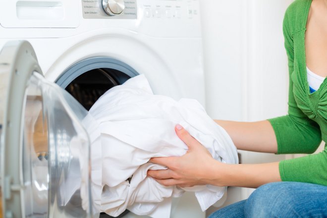 Una mujer poniendo sábanas blancas en la lavadora. 