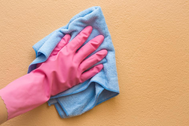 usando un guante rosa y limpiando una pared con un trapo