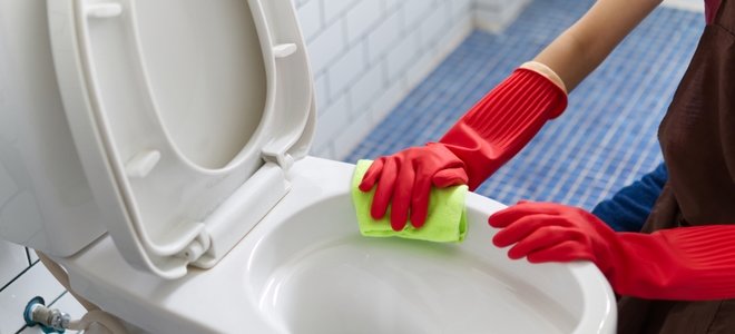 manos en guantes rojos limpiando un inodoro
