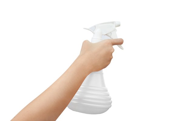 Una botella de spray blanca con una mano sosteniéndola. 