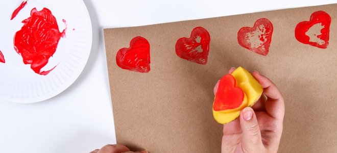 una mano aplicando sellos de corazón rojo a papel marrón