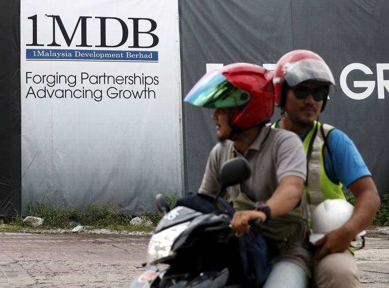 Dos hombres pasan en moto frente a un cartel del fondo soberano 1MDB, en febrero de 2016 en Kuala Lumpur (Malasia).