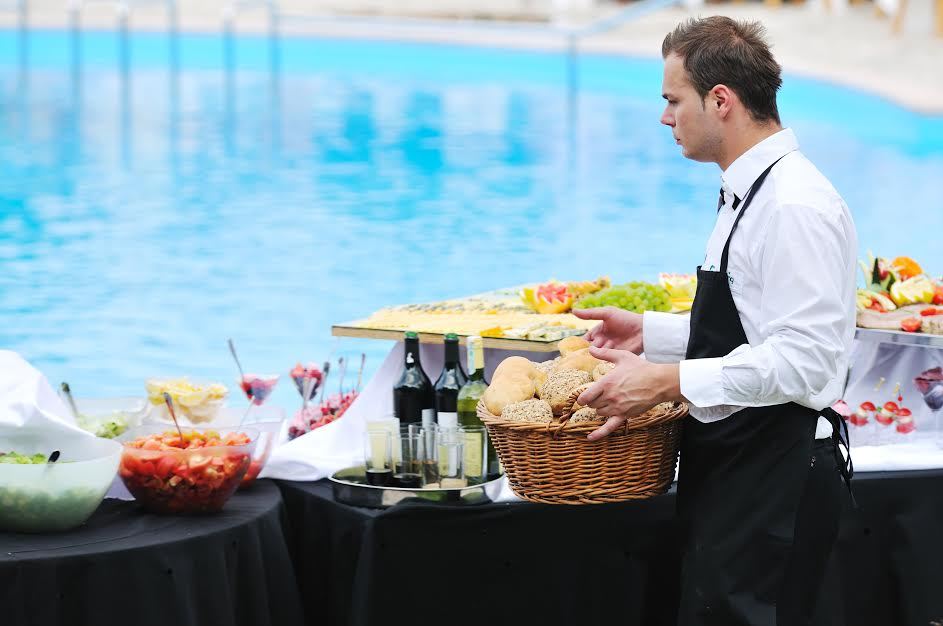 Una empresa de catering que pone la comida en una mesa junto a una piscina. 