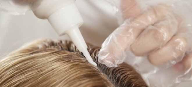 manos enguantadas aplicando tinte para el cabello en el cuero cabelludo