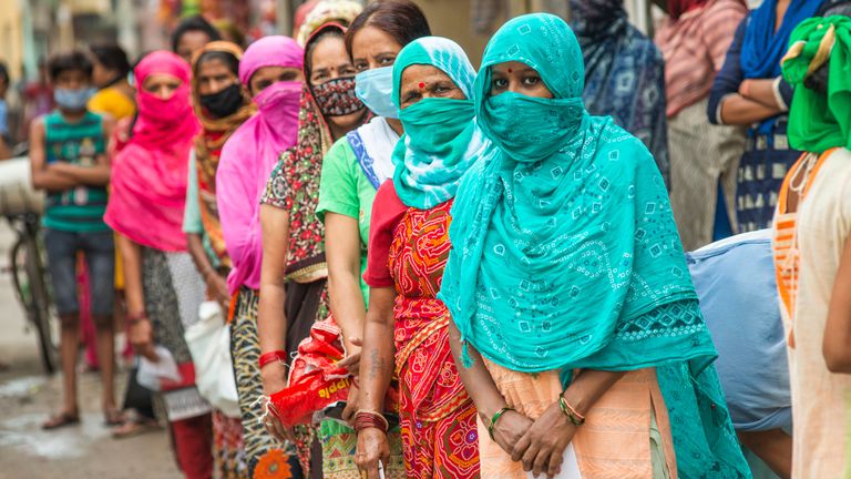 Mujeres indias esperan en una cola de reparto de raciones de comida.