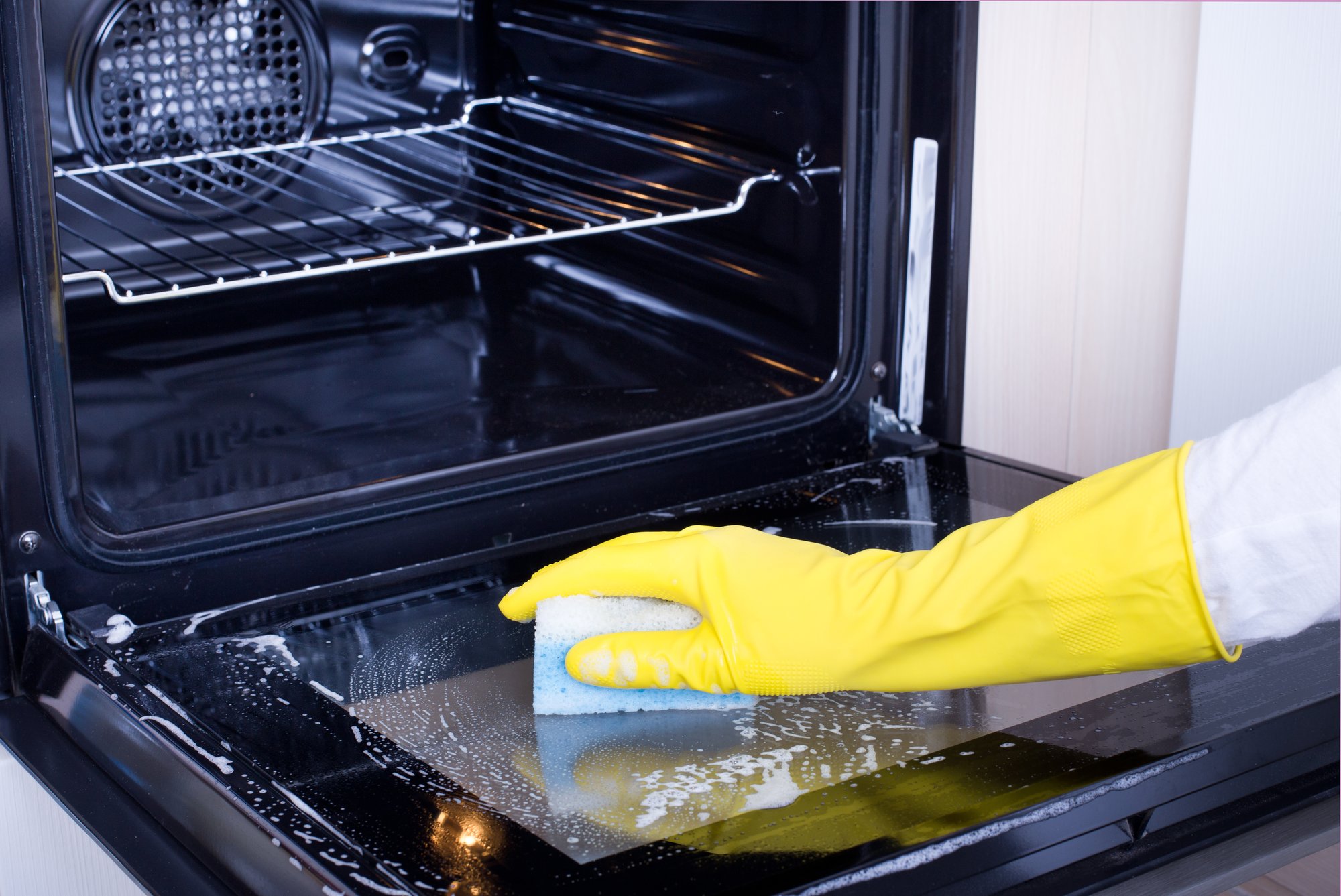 Una mujer con guantes amarillos limpia un horno.
