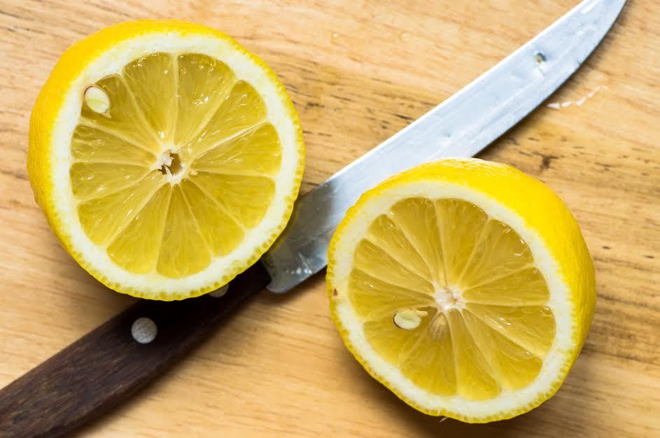 Un limón cortado por la mitad junto a un cuchillo. 