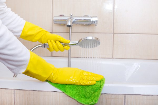 Una persona que limpia una bañera con guantes amarillos. 