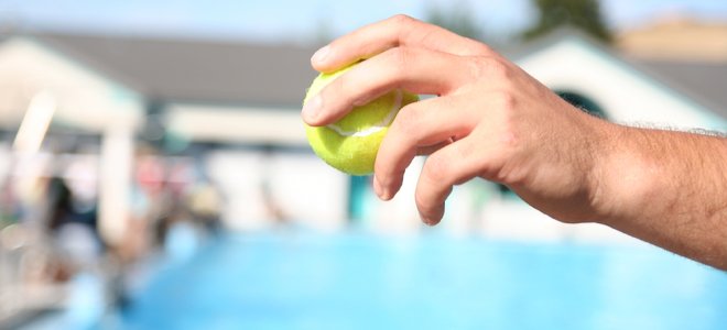 mano sosteniendo una pelota de tenis cerca de la piscina