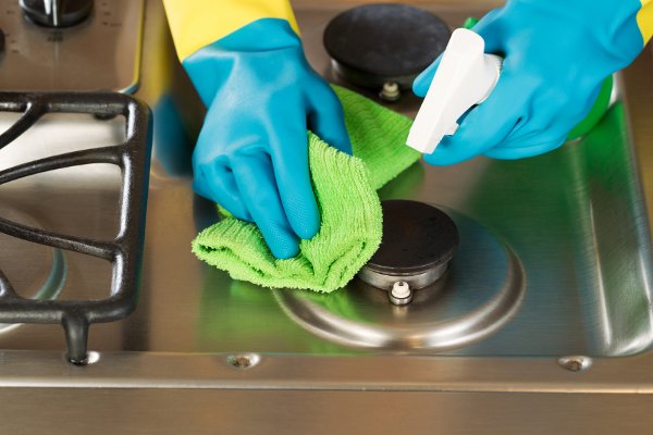 Un par de guantes limpiando una estufa con un trapo y una botella de spray. 