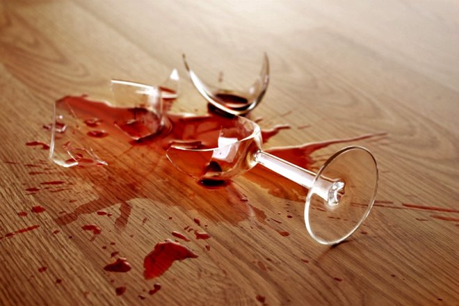 Un vaso roto y vino tinto en un piso de madera.