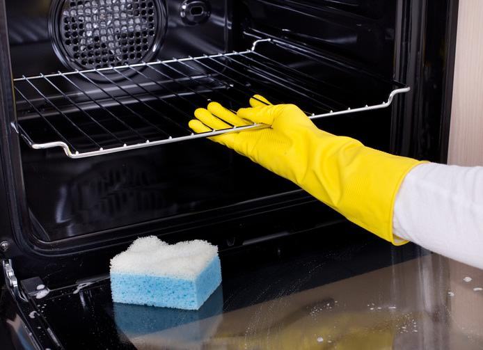 Una mano enguantada limpiando un horno con una esponja. 