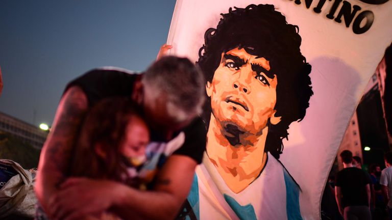 Dos personas lloran la muerte de Maradona junto a una bandera del futbolista, en Buenos Aires.