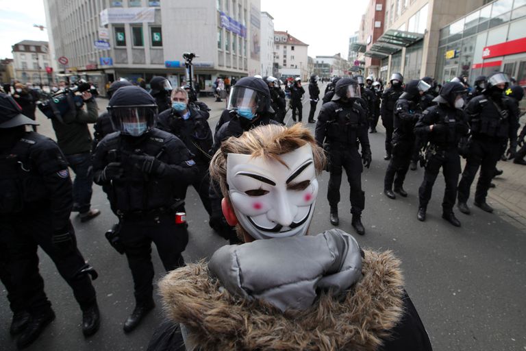 Un manifestante con una máscara de Guy Fawkes se coloca delante de los agentes de policía en Kassel (Alemania), este sábado.