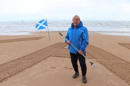 Dougie Bogie escribe con un rastrillo las letras del partido Alba en la playa de Aberdeen.