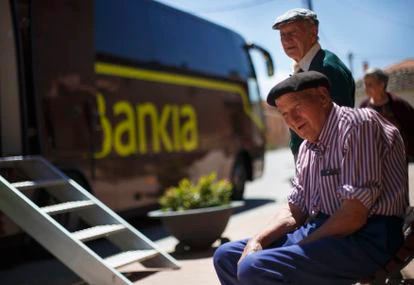 Varios habitantes de Corral de Ayllón (Segovia) hacen cola frente a una oficina móvil de Bankia.