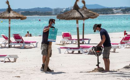 Dos trabajadores preparan la señalización de la playa de Alcudia, en Mallorca, este miércoles.