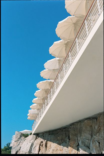 El muro de rocas y la enorme terraza del hôtel du Cap Eden Roc cubierta de sombrillas blancas.