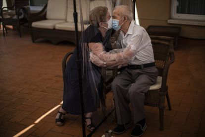 Agustina Cañamero, de 81 años, abraza y besa a su marido, Pascual Pérez, de 84, a través de una pantalla de plástico como medida preventiva contra el coronavirus en una residencia de ancianos en Barcelona, el 22 de junio de 2020.
